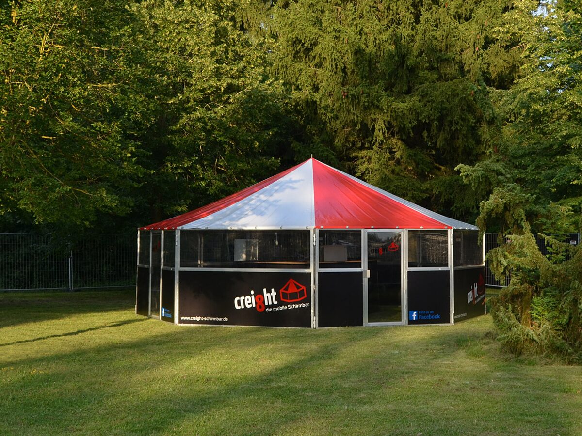 creight Schirmbar von außen bei Tag – achteckige mobile Bar auf einer Festwiese